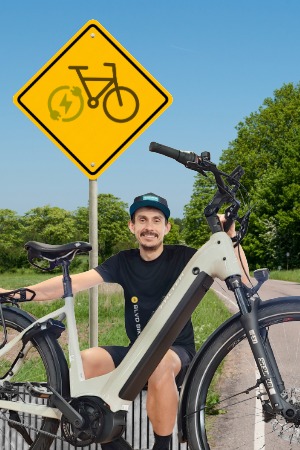Alex sidder med elcykel langs landevej med et elcykel skilt bag sig